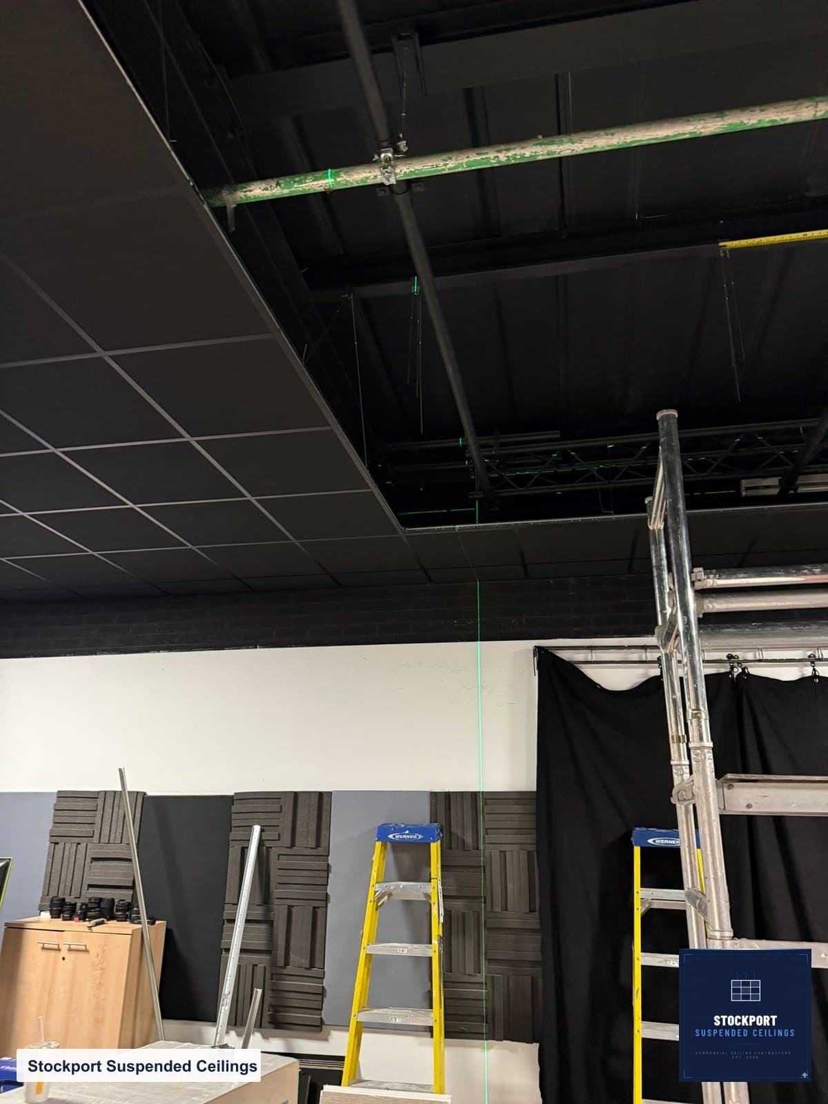 Acoustic ceiling part installed, showing the deep void, long hangers and laser set-out line above the black grid